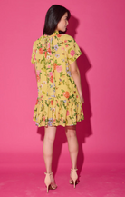 Woman wearing a yellow floral dress against a pink background