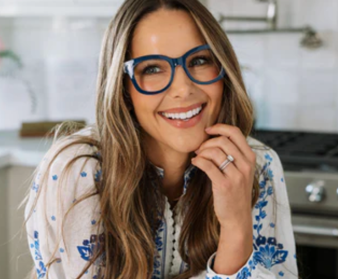 Woman wearing blue glasses and a floral blouse in a kitchen setting