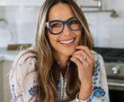 Woman wearing blue glasses and a floral blouse in a kitchen setting