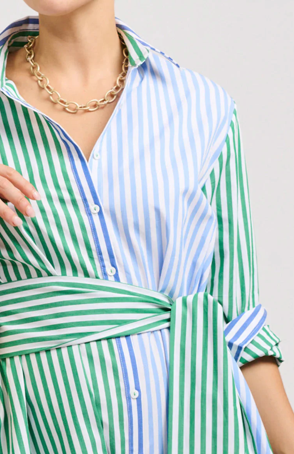 Green and white striped shirt with a gold necklace on a plain background