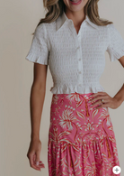 Woman wearing a white smocked top and pink floral skirt on a beige background