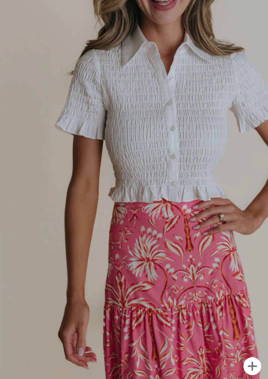 Woman wearing a white smocked top and pink floral skirt on a beige background