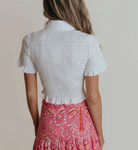 Person wearing a white textured top and pink floral skirt against a plain background