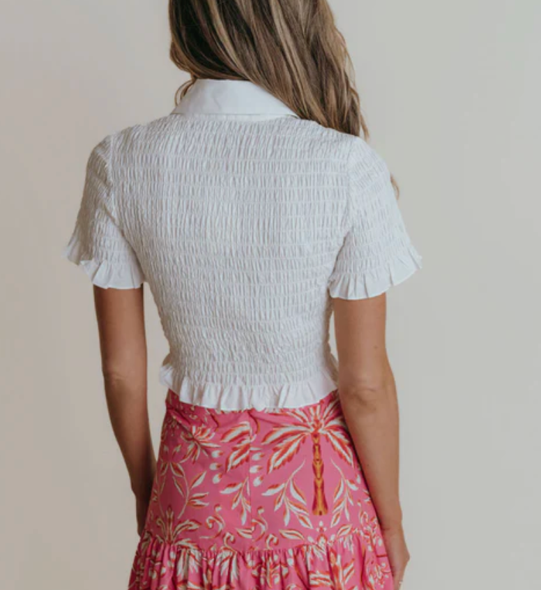 Person wearing a white textured top and pink floral skirt against a plain background
