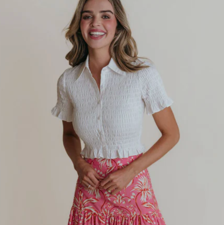 Woman wearing a white short-sleeve blouse and pink patterned skirt against a plain background