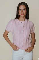 Woman wearing a pink textured blouse and white pants against a plain background