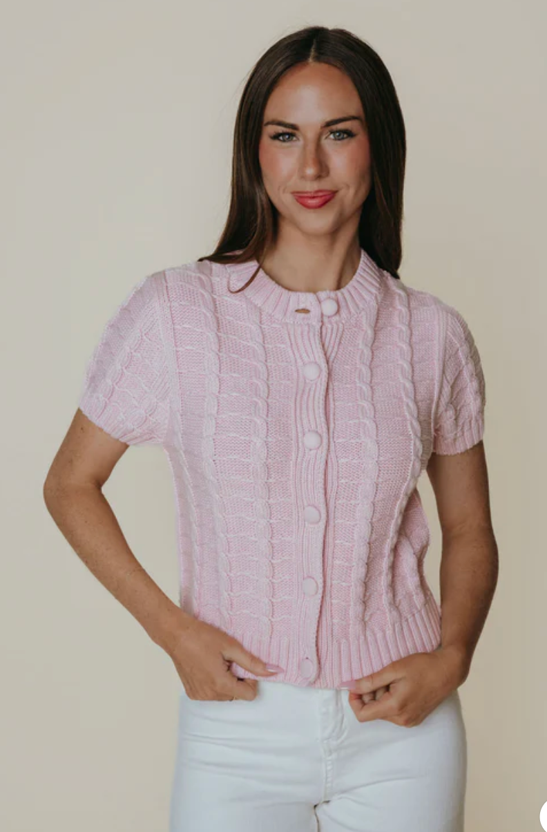 Woman wearing a pink textured blouse and white pants against a plain background