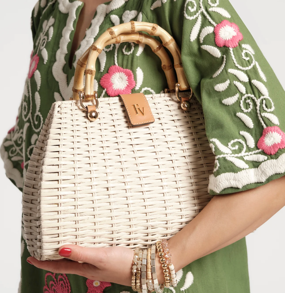 Person holding a woven handbag with a bamboo handle, wearing a green embroidered garment.