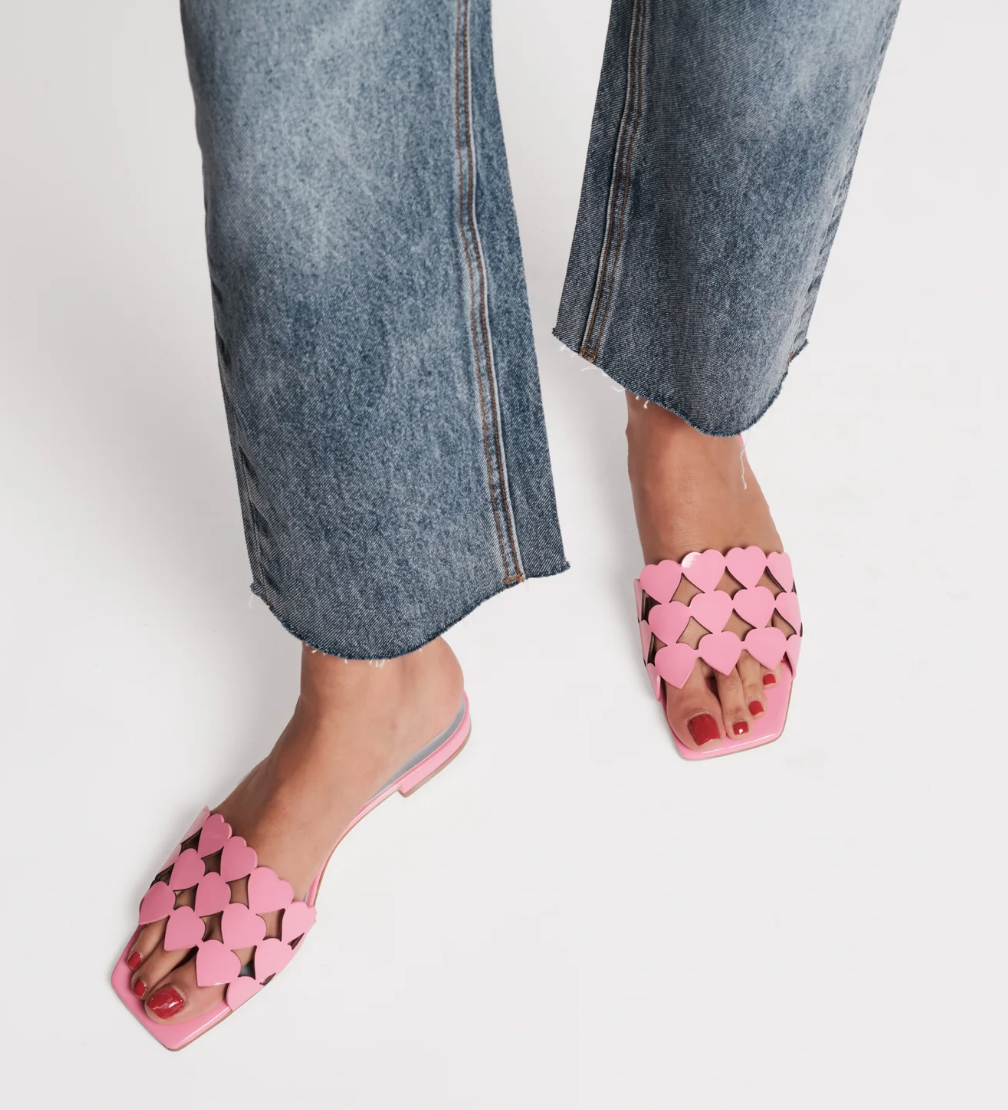 Pink heart-shaped sandals worn with blue jeans on a white background