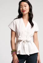 Woman wearing a white blouse with a tie waist on a plain background
