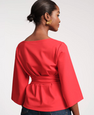 Woman wearing a coral peplum top with a plain background