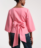 Person wearing a pink top with a bow detail on a plain background
