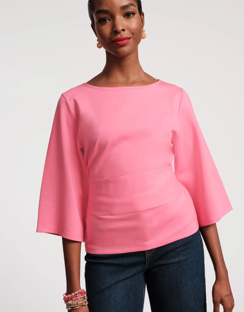 Woman wearing a pink blouse with bell sleeves against a plain background