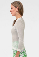 Woman wearing a light gray sweater and green patterned pants on a white background