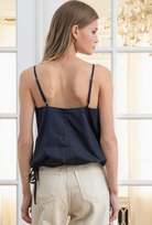Woman wearing a navy blue top with thin straps in a softly lit room.