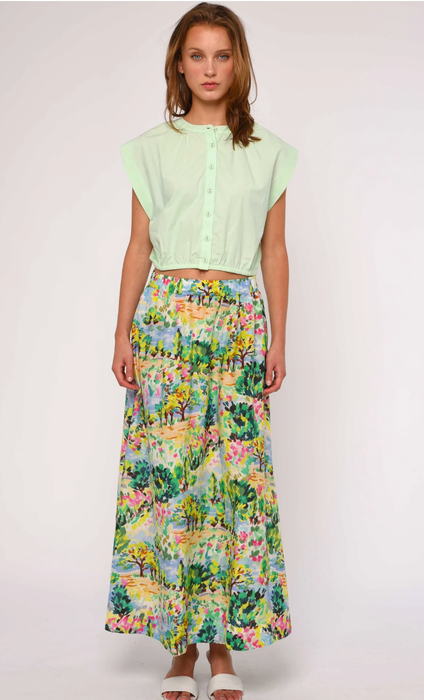 Woman wearing a light green top and a colorful floral skirt on a white background