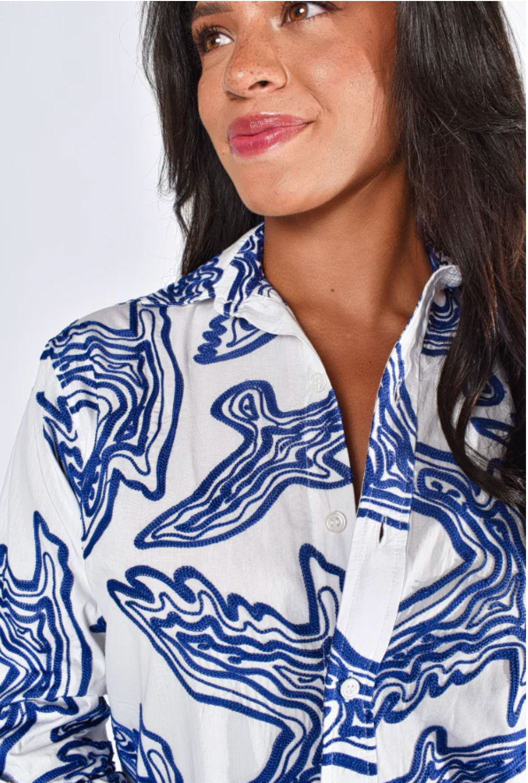 Woman wearing a white shirt with blue abstract patterns on a plain background