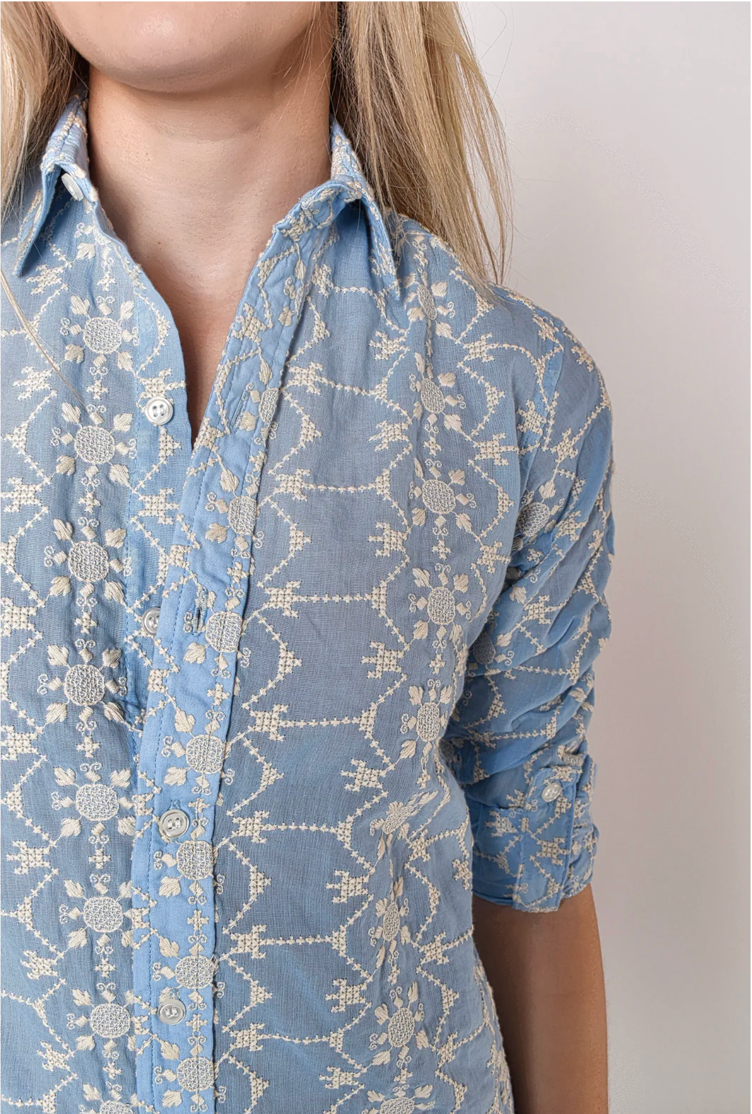 Person wearing a blue patterned shirt with rolled-up sleeves on a plain background