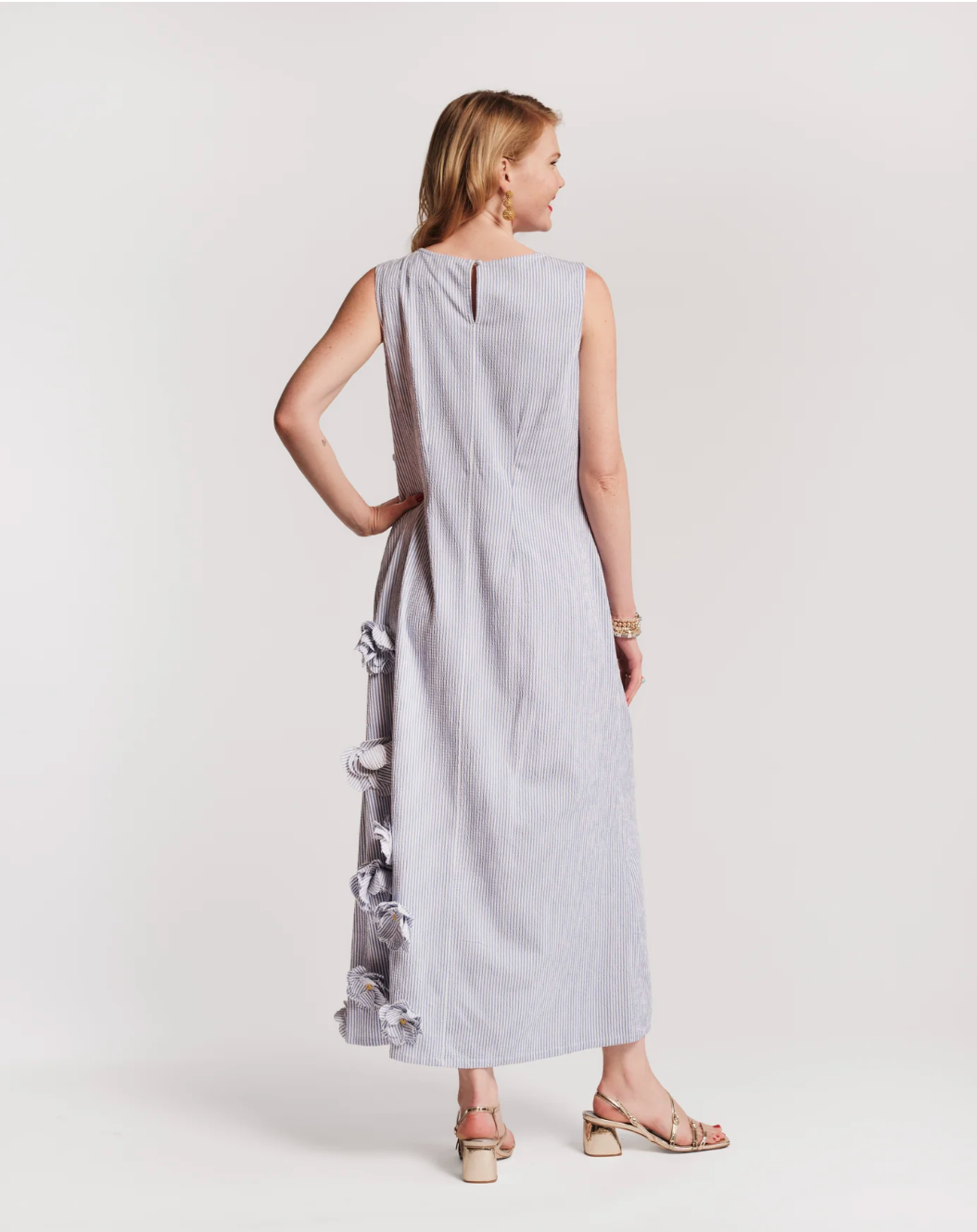 Woman wearing a light gray sleeveless dress holding a baby in a sling against a white background