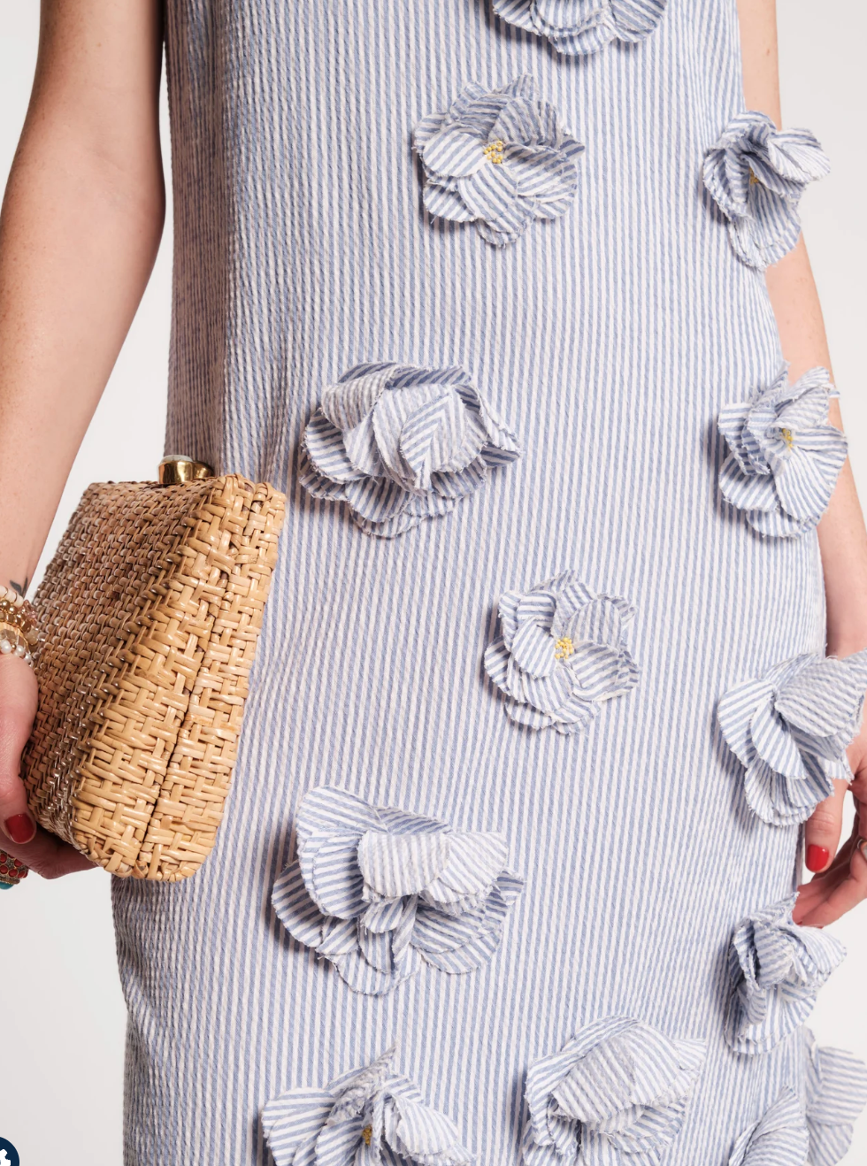 Person wearing a dress with floral patterns holding a woven clutch.