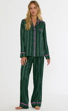 A woman modeling a two-piece green pajama set with vertical stripes and pink piping details, standing against a plain white studio background.
