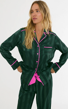 A woman modeling a dark green plaid pajama set with bright pink piping and buttons against a plain white studio background.