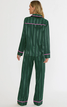 A woman modeling a dark green satin pajama set with vertical stripes and bright pink piping, shown from the back against a plain white studio background.