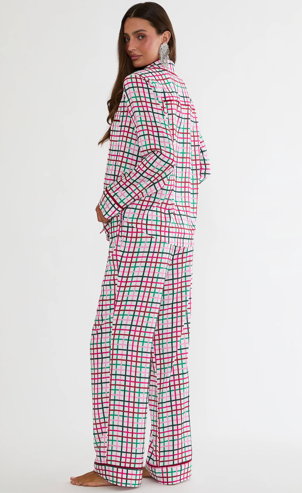 A woman modeling a matching two-piece pajama set with a red, green, and black plaid pattern on a white background, shown from a side-back angle against a plain white studio backdrop.