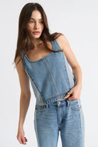 Woman wearing a denim sleeveless top and jeans on a white background