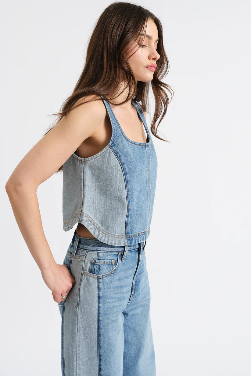 Woman wearing a denim sleeveless top and jeans on a white background