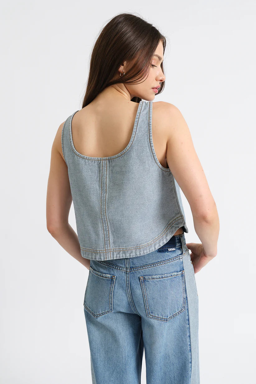 Woman wearing a light blue denim tank top and jeans on a white background