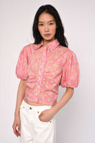 Woman wearing a pink floral blouse with white pants on a plain background