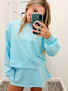 A woman takes a mirror selfie wearing a light blue matching lounge set consisting of a long-sleeve sweatshirt and a short skirt, both decorated with tiny white polka dots.