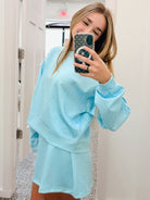 A woman takes a mirror selfie wearing a light blue matching lounge set with small white polka dots, consisting of a sweatshirt and shorts, in a hallway.
