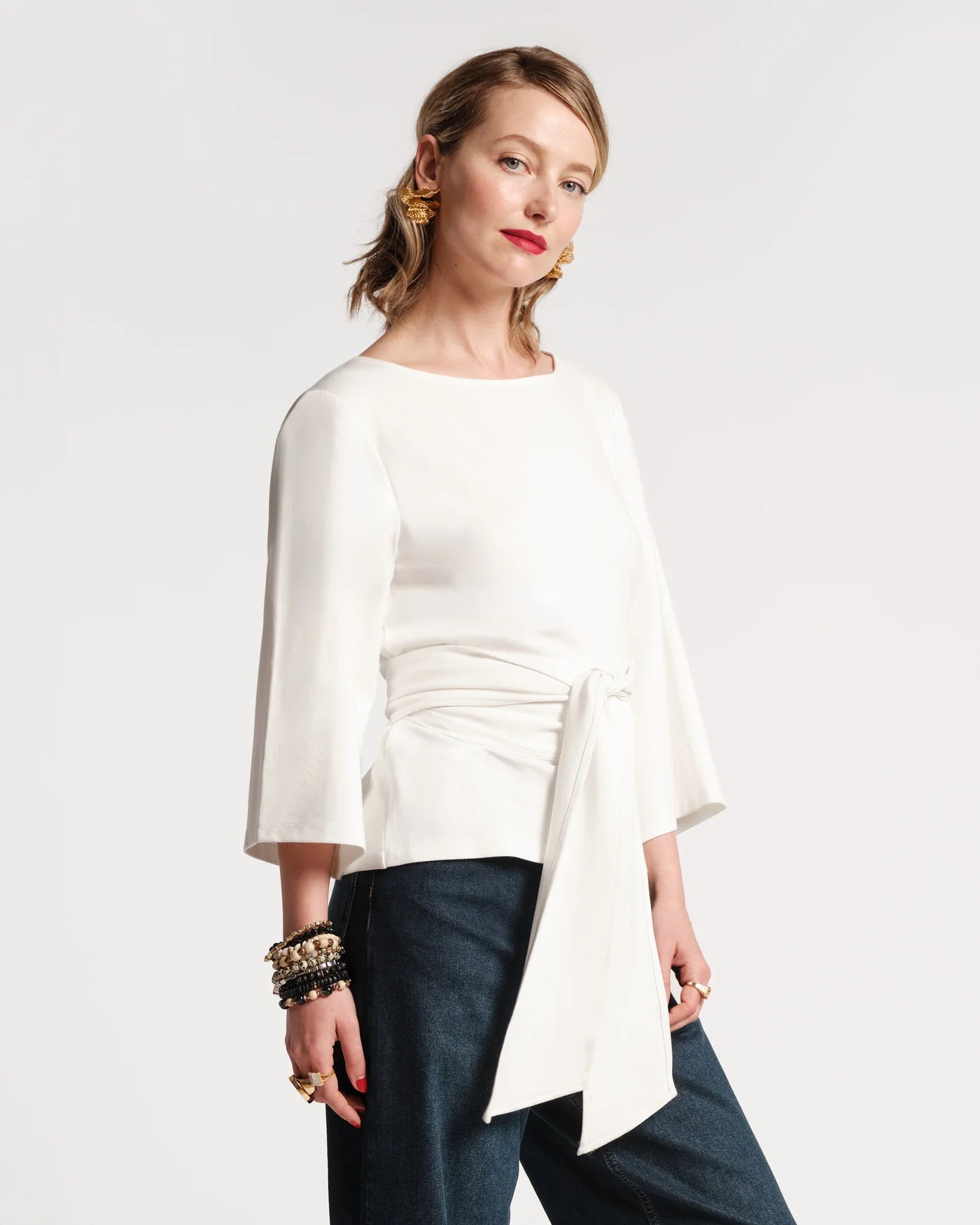 Woman wearing a white blouse with a ruched design and dark pants on a white background