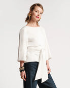 Woman wearing a white blouse with a ruched design and dark pants on a white background