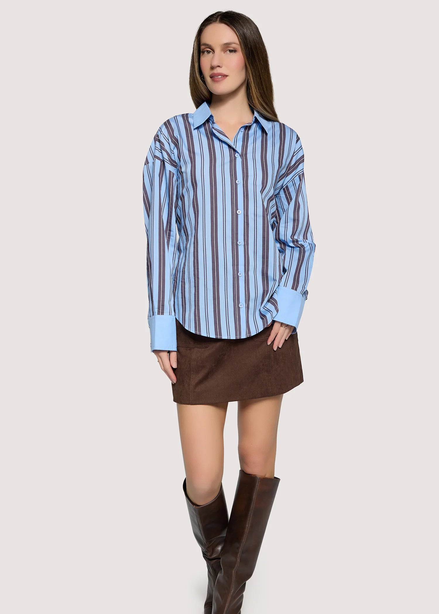 Woman wearing a blue striped shirt, brown skirt, and brown boots on a white background