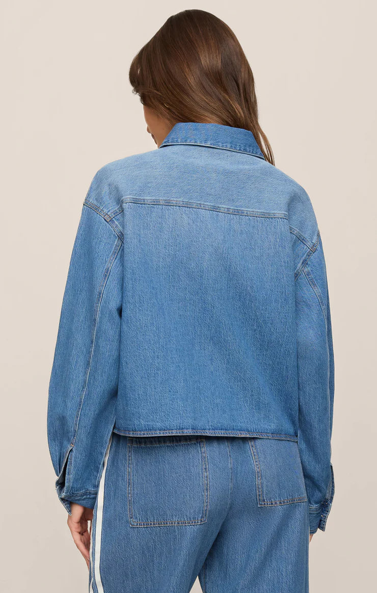 Person wearing a blue denim jacket and pants on a beige background