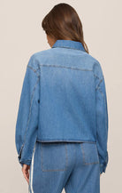 Person wearing a blue denim jacket and pants on a beige background