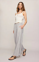 Woman wearing a white sleeveless top and striped pants on a plain background