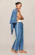 Woman wearing a denim jacket and blue pants with white stripes on a beige background