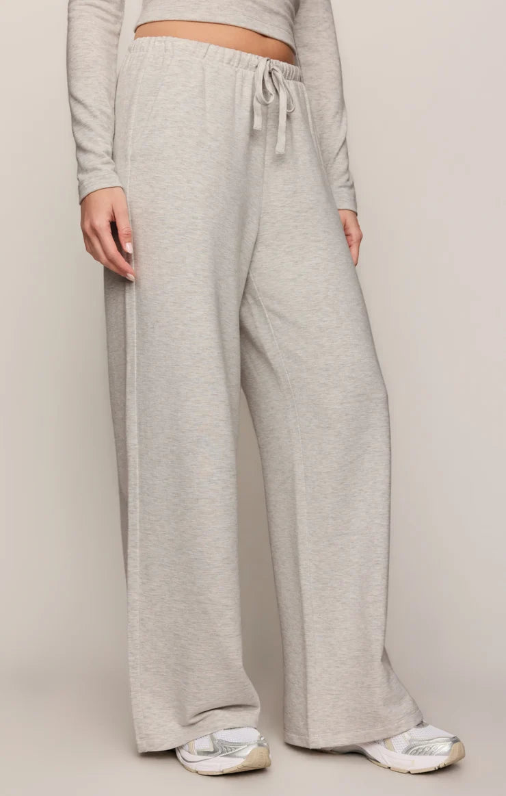 A person wearing light heather gray wide-leg sweatpants with an elastic drawstring waist, paired with a matching long-sleeve crop top and white sneakers, against a plain light beige studio background.
