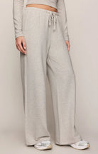 A person wearing light heather gray wide-leg sweatpants with an elastic drawstring waist, paired with a matching long-sleeve crop top and white sneakers, against a plain light beige studio background.