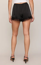 Black satin shorts with a lace hem, modeled from the back against a neutral beige background.