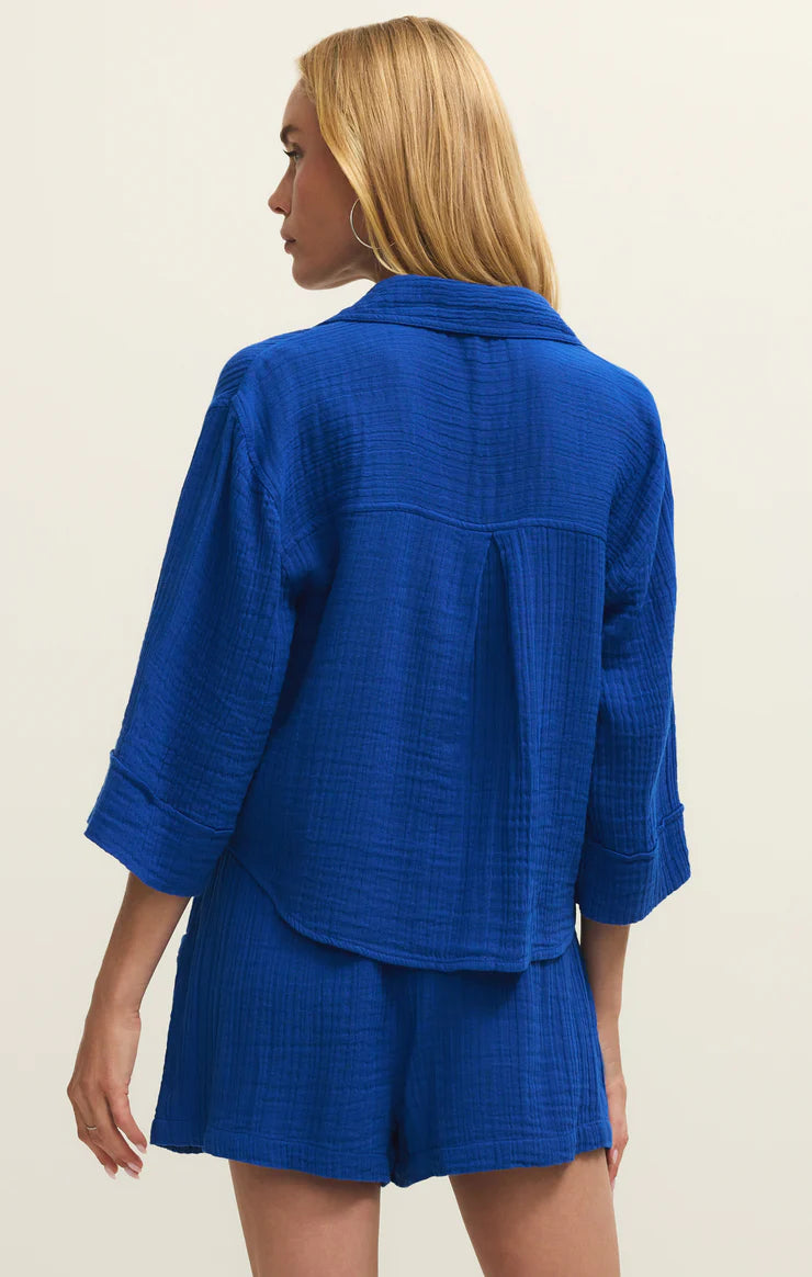 Woman wearing a blue textured outfit with a jacket and shorts on a beige background