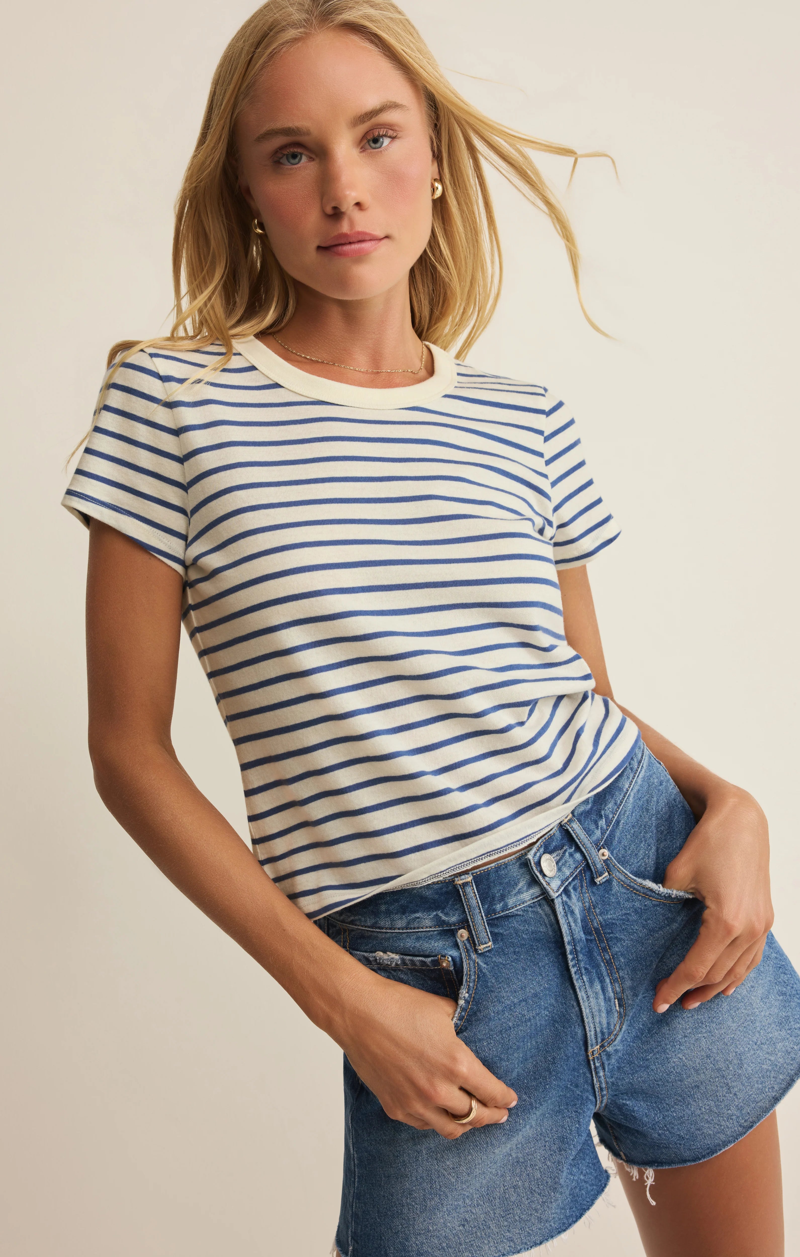 Woman wearing a striped shirt and denim shorts against a neutral background