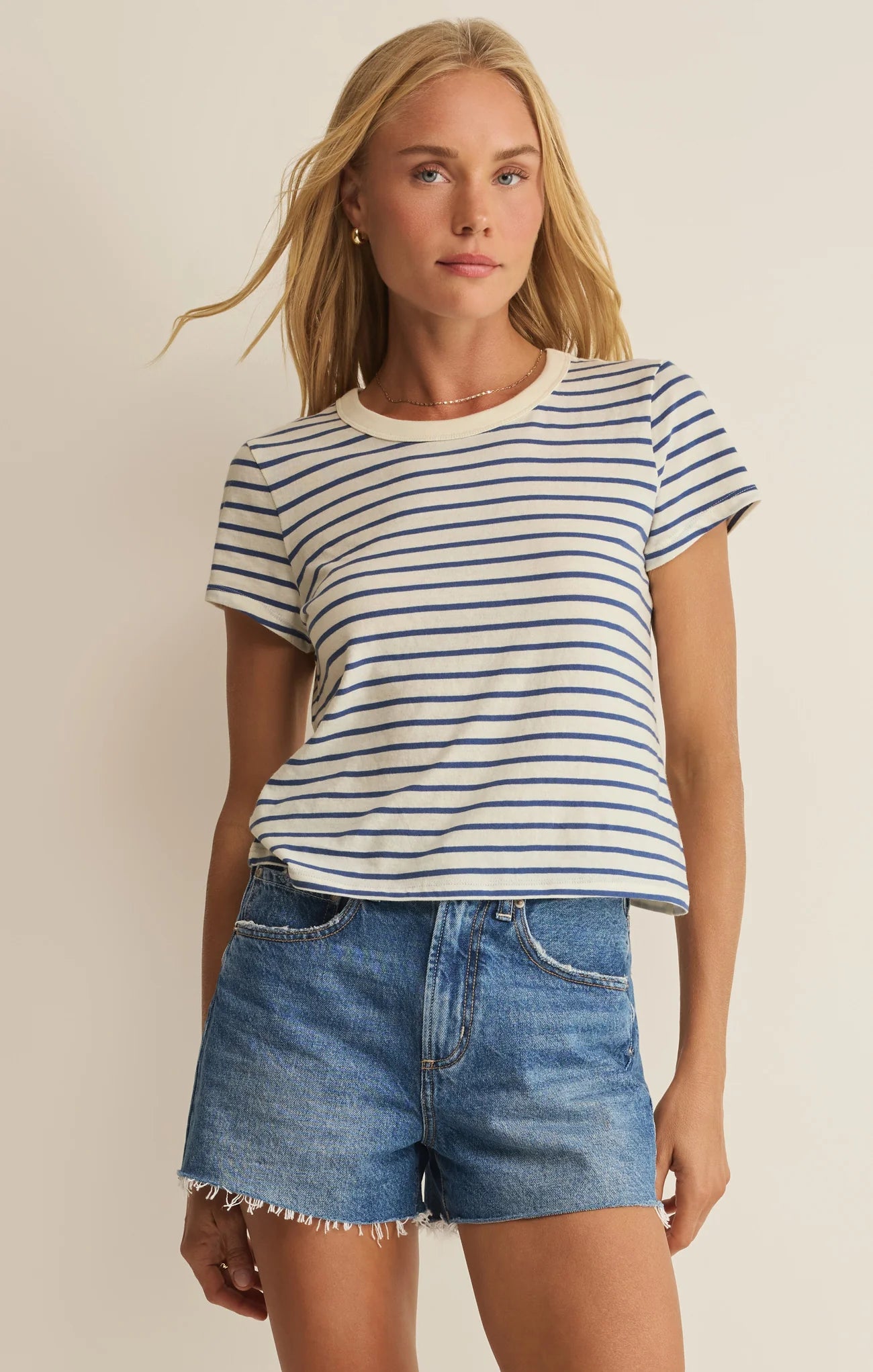 Woman wearing a striped shirt and denim shorts against a beige background