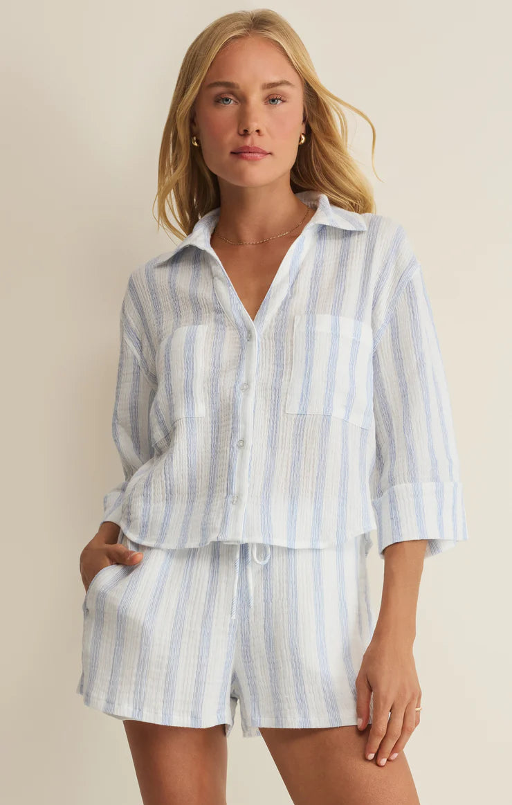 Woman wearing a light blue and white striped shirt and shorts set against a beige background