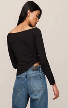 Woman wearing a black long-sleeve top and blue jeans on a beige background