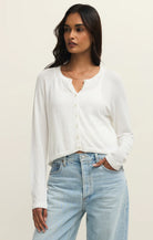 Woman wearing a white cardigan and light blue jeans against a plain background